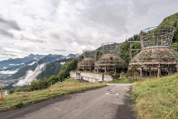 Three abandoned dismantled cooling towers in the mountains with a cloudy sky and a road alongside.