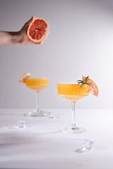 Two orange coctails and hand holding grapefruit on white background