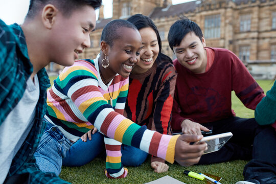 Group of young university students hanging out on grass studying and viewing mobile device