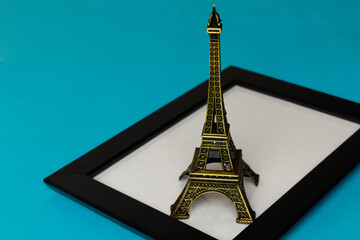 The concept of travel and tourism with a photo frame. The Eiffel Tower stands on a stylish black photo frame with glass on a turquoise background. A place for your photo or text. Side view from above