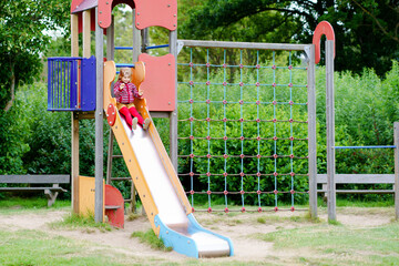 Little preschool girl playing on outdoor playground. Happy toddler child climbing and having fun...