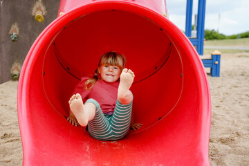 Little preschool girl playing on outdoor playground. Happy toddler child climbing and having fun...
