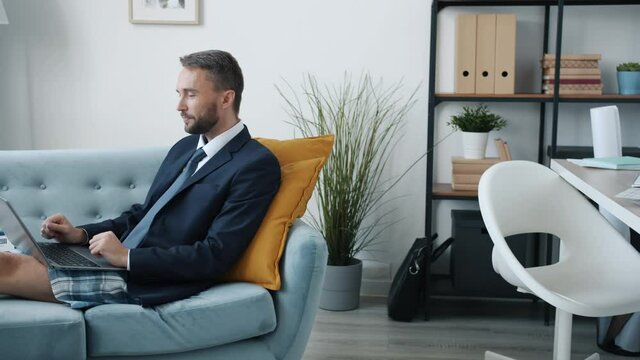 Motivated businessman in pajamas shorts and forman jacket is making video call working online from home during lockdown. People and technology concept.