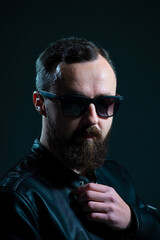 Fototapeta premium dramatic portrait of bearded millennial guy in leather jacket on dark background