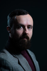 Fototapeta premium a dramatic portrait of a bearded millennial guy in a jacket and sweater. On a dark background