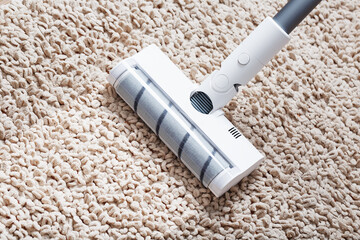 A cordless vacuum cleaner cleans the carpet in the living room with the bottom of the legs With a...