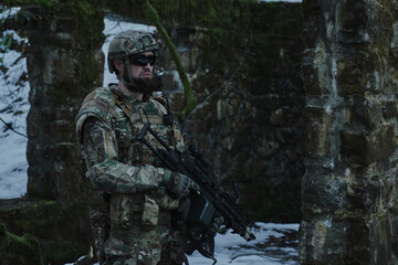 Fototapeta premium Portrait of airsoft player in professional equipment with machine gun in the forest. Soldier with weapons at war