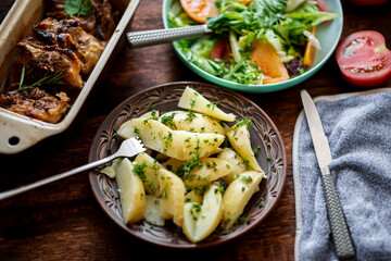Boiled young potatoes with dill, fresh vegetable salad and baked chicken thighs on a dark wooden background.