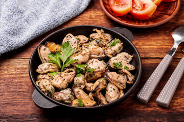 Peeled mussels in sauce on a dark wooden background.