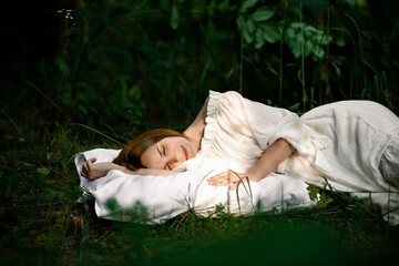 Healthy sound sleep. Rest, relaxation in the forest. Woman sleeps on a pillow on a green glade in...