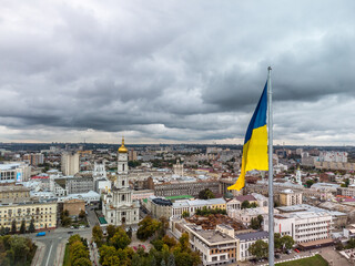 Flag of Ukraine close-up with autumnal epic gray cloudscape, city aerial view near river Lopan embankment, Dormition Cathedral in Kharkiv, Ukraine