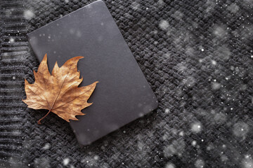 Herbstheim cozy composition. Dried autumn leaf on a book, on a dark scarf background. Flat lay.