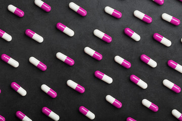 A pattern of pink and white medical pills on a black background