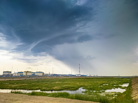 A Large Storm Cloud With Rain Over The Green Tundra And Industrial Buildings