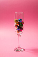 Glass full of Christmas colorful decoration. Pink background. Shine look.