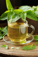 Lemon balm herbal tea in glass cup with fresh plant close, melissa officinalis herb is used for sleep, as digestive, anxiety, stress remedy, closeup, naturopathy and natural medicine concept - obrazy, fototapety, plakaty