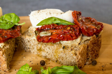 Bruschetta with sun-dried tomatoes, mozzarella and basil, served on a wooden plate.
