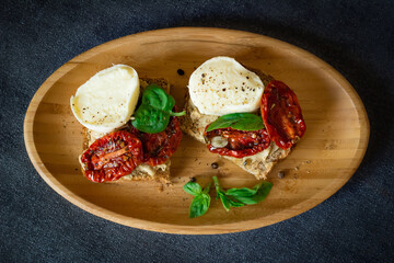 Bruschetta with sun-dried tomatoes, mozzarella and basil, served on a wooden plate.
