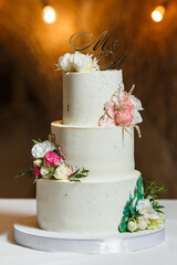 Elegant white wedding cake decorated with fresh flowers and gold topper.