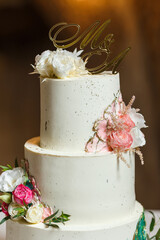 Elegant white wedding cake decorated with fresh flowers and gold topper.
