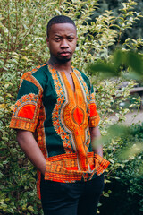 Young African man walking in the park. Handsome young man with brown skin. Stylish black man with afro hair wearing a fashionable african print danshiki