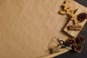 Simple minimalistic Christmas composition with handmade gingerbread biscuits and present decorated with pine cone and tied cinnamon in a bow with a rope on a brown craft wrapping paper with copy space