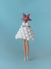 Doll legs with artificial Christmas tree made of balls with false eyelashes and pink star on pastel blue background. Creative minimal fashion concept. New year and merry christmas inspiration.