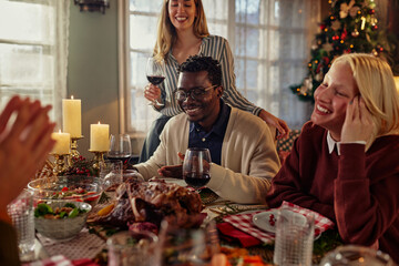 Group of diverse friends sitting at the dining table and enjoying Christmas lunch