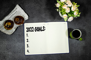 Notebook with empty to-do list for 2022 year, cup of coffee and macarons cookies, flowers pot