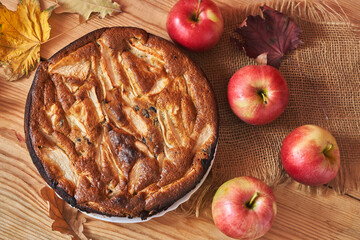 Naklejka na ściany i meble Freshly baked apple pie on a wooden table next to red apples and autumn leaves