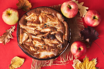 Freshly baked apple pie on a wooden table next to red apples and autumn leaves