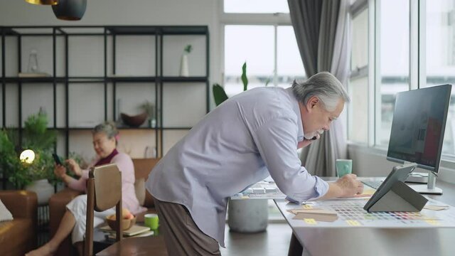 old asian senior retired age working at home hand ise desktop  and paper document at working desk in living room home interior background,asian male senior work at home