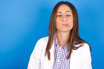 young european doctor girl wearing white medical gown ​on white background  making grimace and...