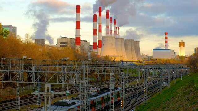 Smoke from the pipes of heat station against the background of a cloudy sky and MCC electric train. Ecological energy concept. 