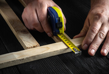 The carpenter uses a construction tape to measure the length of a piece of wood. Hands of the...
