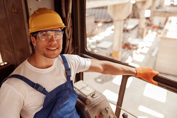 Cheerful man sitting in operator cabin of industrial crane