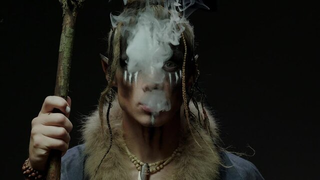 Inspired elf shaman breathes out smoke standing on black