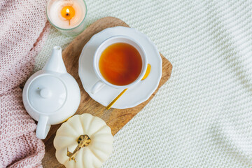 Autumn flat lay. Orange knitted pullover, hot cup of tea, candle light, wooden stand, cotton branch, pumpkin.