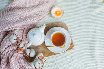 Autumn flat lay. Orange knitted pullover, hot cup of tea, candle light, wooden stand, cotton branch, pumpkin.