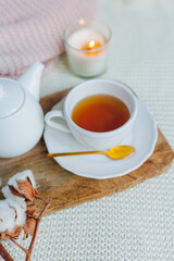 Autumn flat lay. Orange knitted pullover, hot cup of tea, candle light, wooden stand, cotton branch, pumpkin.