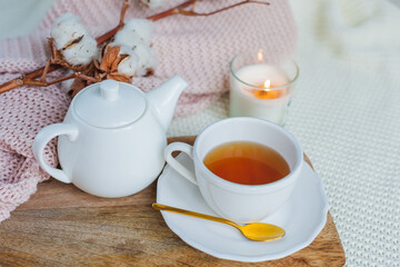 Autumn flat lay. Orange knitted pullover, hot cup of tea, candle light, wooden stand, cotton branch, pumpkin.