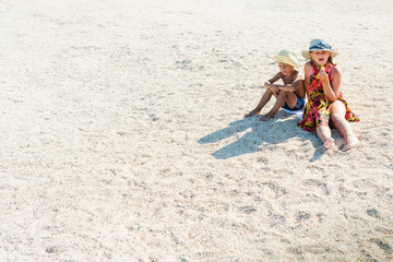 relaxing in the air, a blond boy and a blond girl in hats sitting on the beach, on the sand and eating or tasting ice cream with a small depth of field and copy space. Vacation concept 