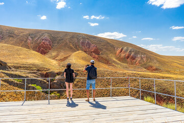 Family couple travelers walking in mountain area. Rear view of man and woman standing on trail against Martian landscapes of red hills. Bogdo Baskunchak Nature Reserve, Astrakhan region, Russia