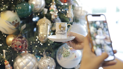 joven tomando una foto con su teléfono móvil de una taza de navidad decorada con un fondo de árbol borroso. concepto de decoración de navidad