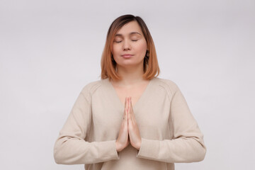 Calm young woman meditating, show namaste pray gesture, close eyes and smiling, making wish, pleading god, standing over white background