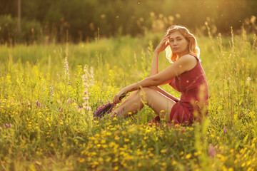 Naklejka na ściany i meble A beautiful girl with a bouquet of lupines is sitting in a field of small yellow flowers