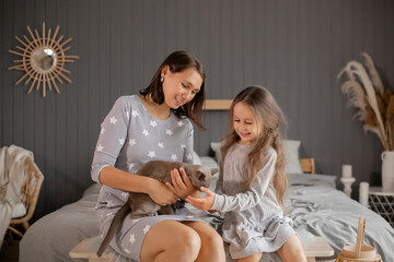 Mom and daughter play with a cat while sitting on the bed - Powered by Adobe