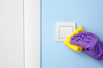 Woman cleaning switch on blue wall, closeup
