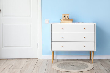 Chest of drawers with calendar and books near blue wall
