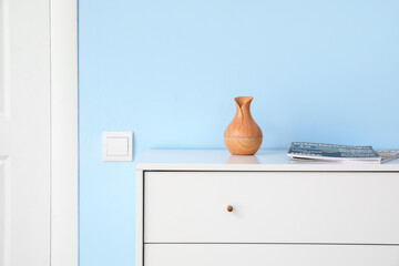 Chest of drawers with vase and magazines near blue wall